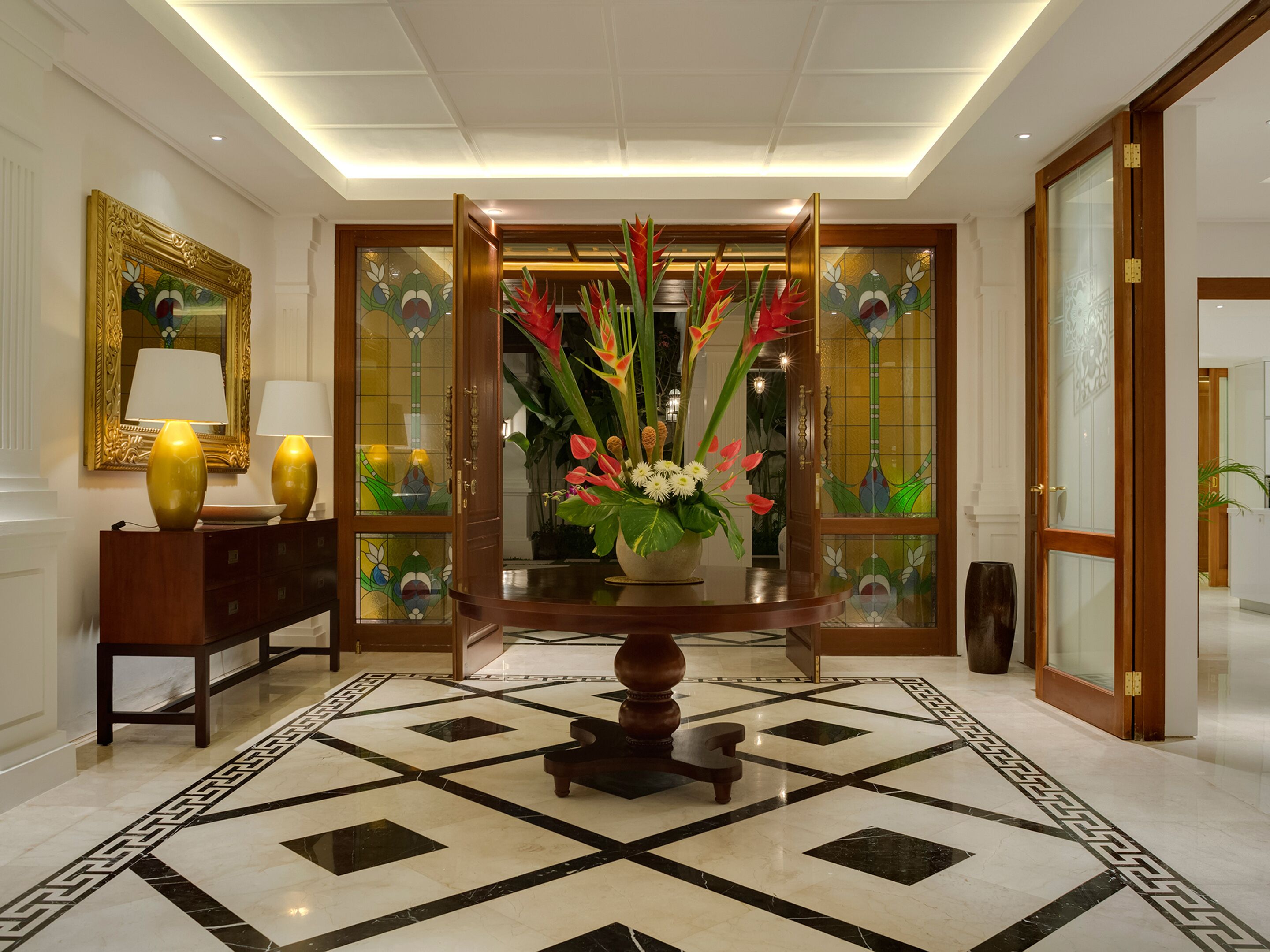 En lobby med et marmorgulv, en træreception, en blomstervase og et stort spejl med gylden ramme.