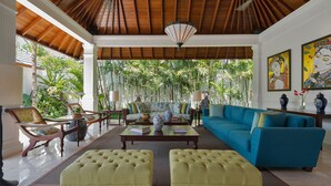 A spacious living area with a high wooden ceiling, a blue sofa, two yellow ottomans, and a wooden coffee table. - Villa Windu Asri (Seminyak)