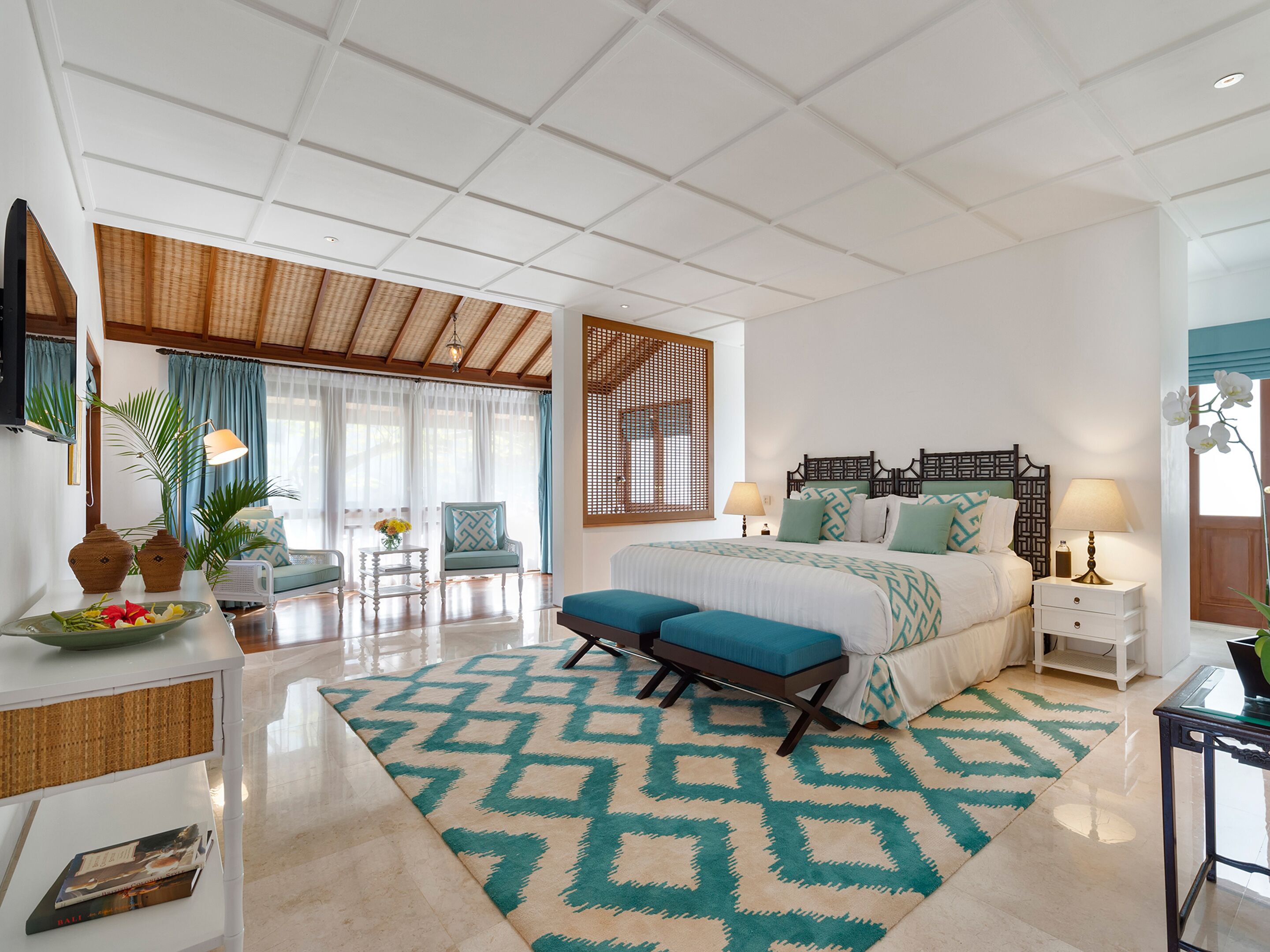 Un dormitorio amplio con una cama grande, un rincón de descanso con una silla y una mesa, y un panel decorativo en la pared.