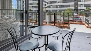 Un balcon avec une table et des chaises, une porte vitrée et une vue sur un immeuble moderne.