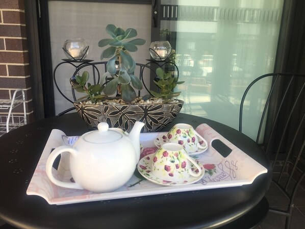 Een tafel met een theepot en theekopjes op een dienblad, een decoratieve plant en een raam met uitzicht.