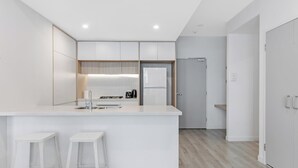 Une cuisine moderne avec des meubles blancs, un îlot central doté de tabourets et une porte donnant sur une autre pièce.