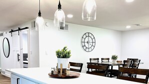 Et moderne køkken med en stor ø, hvide skabe og hængende lamper.