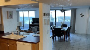 A modern kitchen with a dishwasher, a dining area with a table and chairs, and a large window offering a view of the city. - 12th Floor Oceanfront South End Unit overlooking Daytona (Daytona Beach)