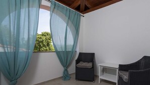 A balcony with teal curtains, a wicker chair, a white table, and a view of greenery. - Holiday House Stone Lady (Rasopasno)
