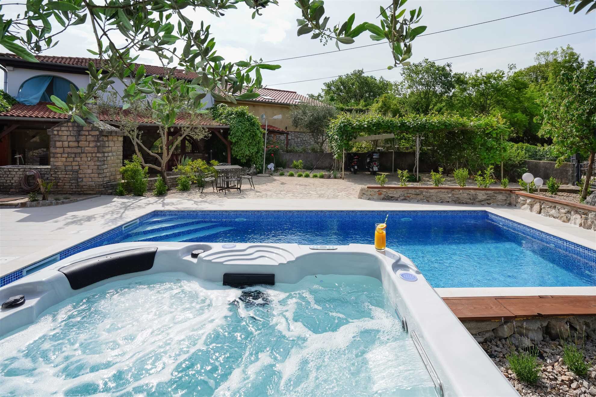 A swimming pool with a hot tub, surrounded by a stone wall and greenery.