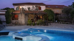 A swimming pool with hot tubs, surrounded by a stone patio and a house with a tiled roof. - Holiday House Stone Lady (Rasopasno)