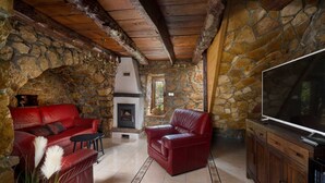 A cozy stone-walled room with a fireplace, red leather sofas, a TV, and a tiled floor. - Holiday House Stone Lady (Rasopasno)