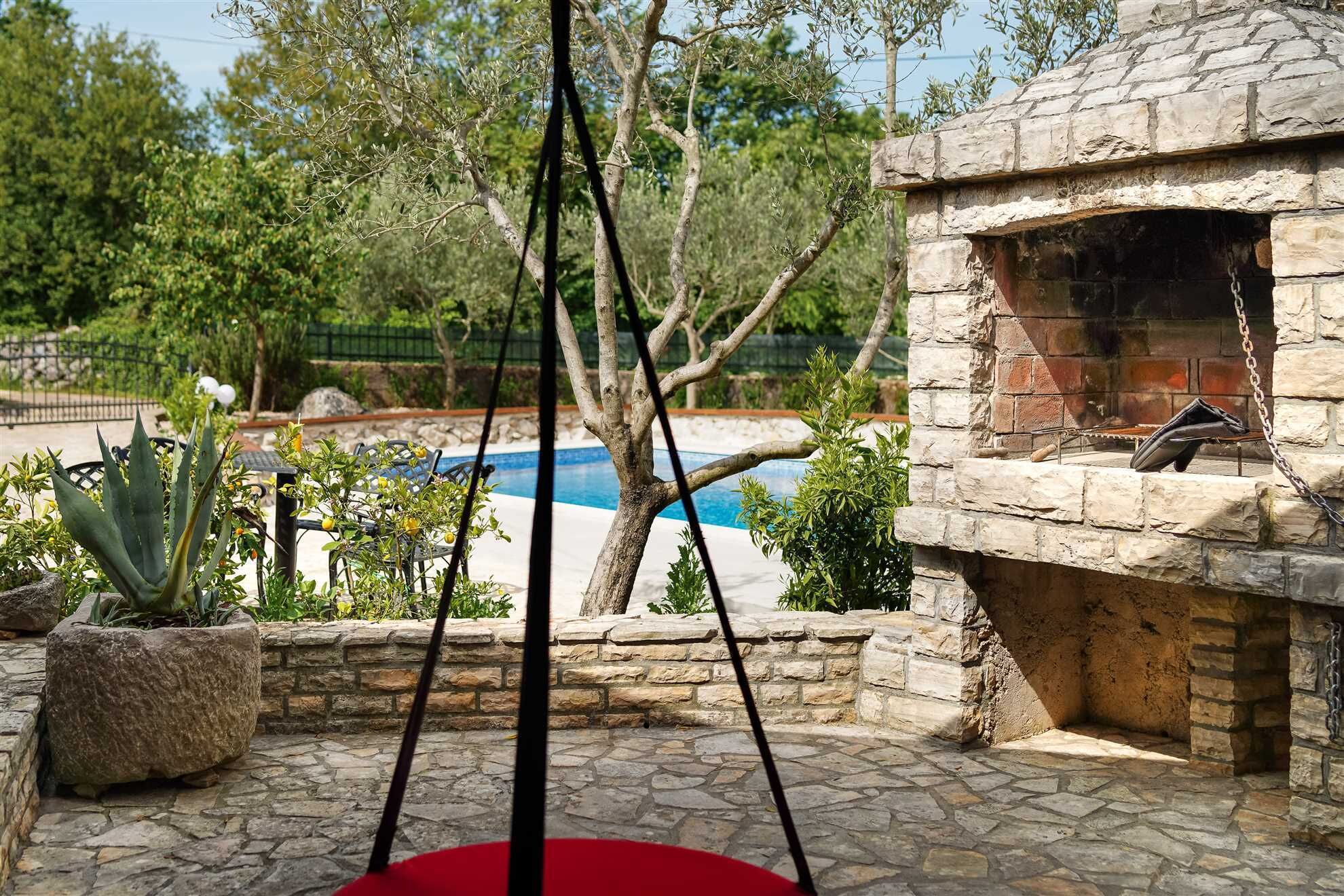 Eine Terrass mit Kamin aus Stein, Pool und verschiedenen Pflanzen.