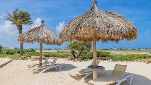 Une plage avec des parasols en chaume et des chaises longues.