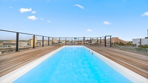 A rooftop swimming pool with wooden decking and a clear view of the cityscape in the background. - NEW 2BR Condo in  of Palm Beach! Walk 2 Beach! (Palm Beach)