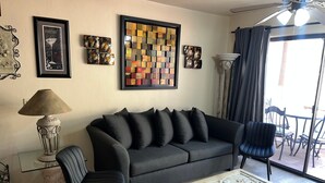 A living room with a black sofa, a glass coffee table, a lamp, and artwork on the walls.