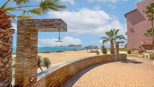 A beachfront hotel with a stone archway, palm trees, and a clear view of the ocean.