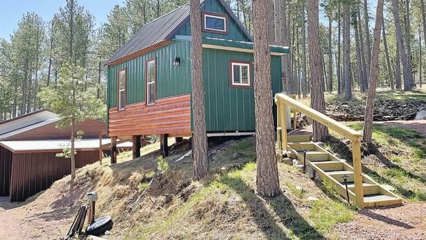 Eine Holzhütte mit einer Holzterrasse und einer Treppe, die zu ihr hinaufführt, umgeben von Bäumen.