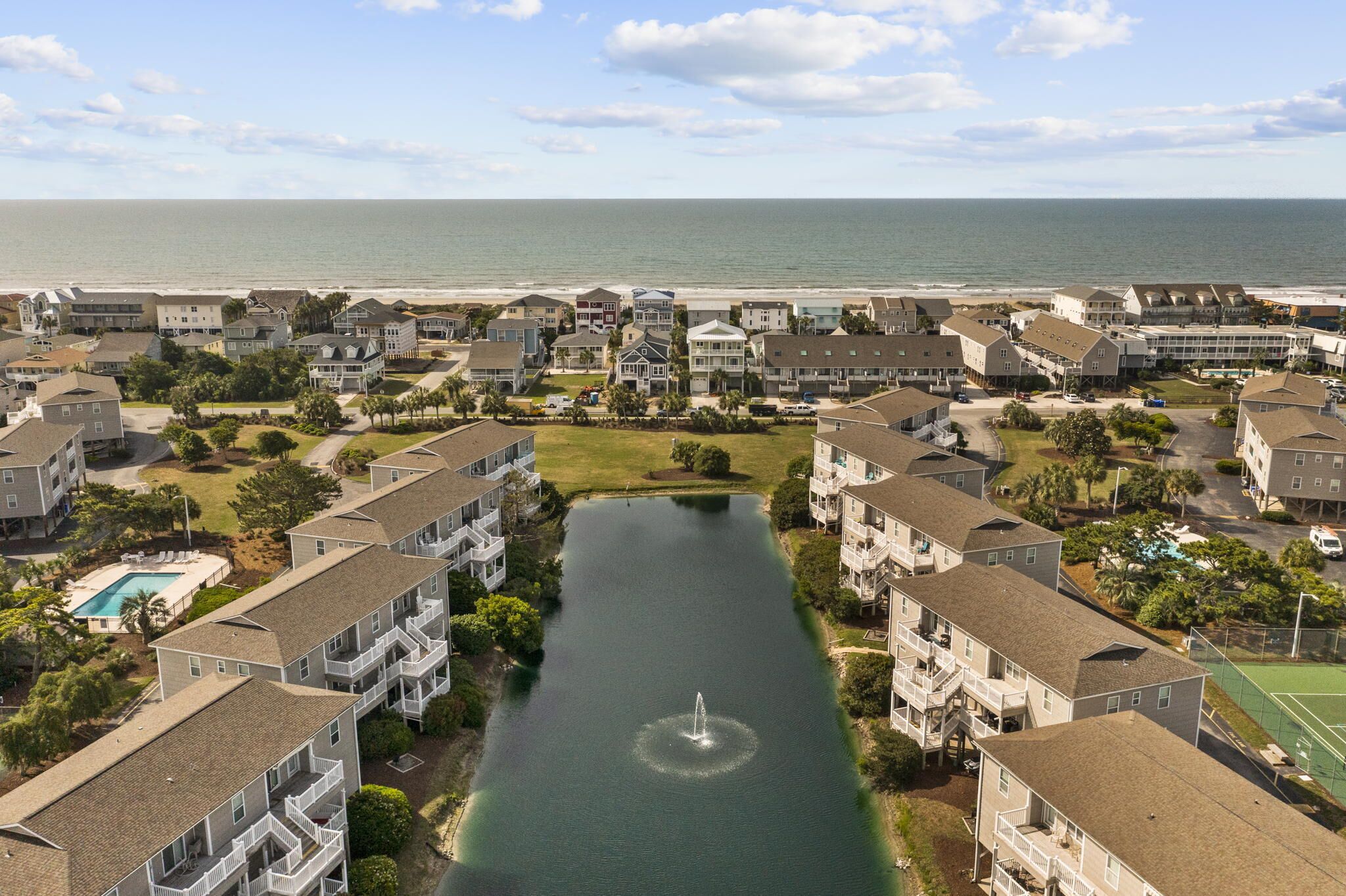 Zona residencial com um espelho de água central, rodeada por edifícios altos com varandas, piscina e vista para o oceano.