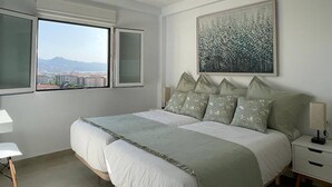 A bedroom with a large bed, two windows, a painting, and a nightstand.