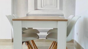 A modern dining area with a long table and chairs, leading to a corridor with a repeating pattern on the walls.