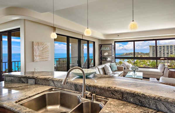 A modern kitchen with a granite countertop, stainless steel sink, and a view of the ocean through large windows.