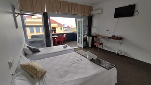 A hotel room with two beds, a desk, a TV, and a balcony with a view of the city. - Ayr Hotel (Ayr)