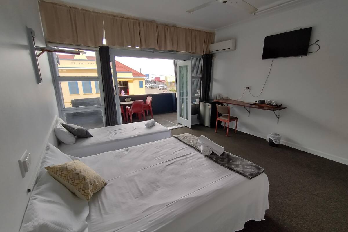 A hotel room with two beds, a desk, a TV, and a balcony with a view of the city.