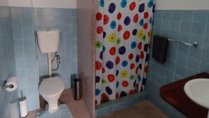 A bathroom with a toilet, a shower curtain with a colorful flower pattern, a sink, and blue tiled walls. - Ayr Hotel (Ayr)