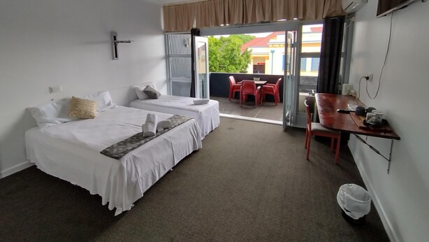 A hotel room with two beds, a ceiling fan, a balcony with red chairs, and a table. - Ayr Hotel (Ayr)