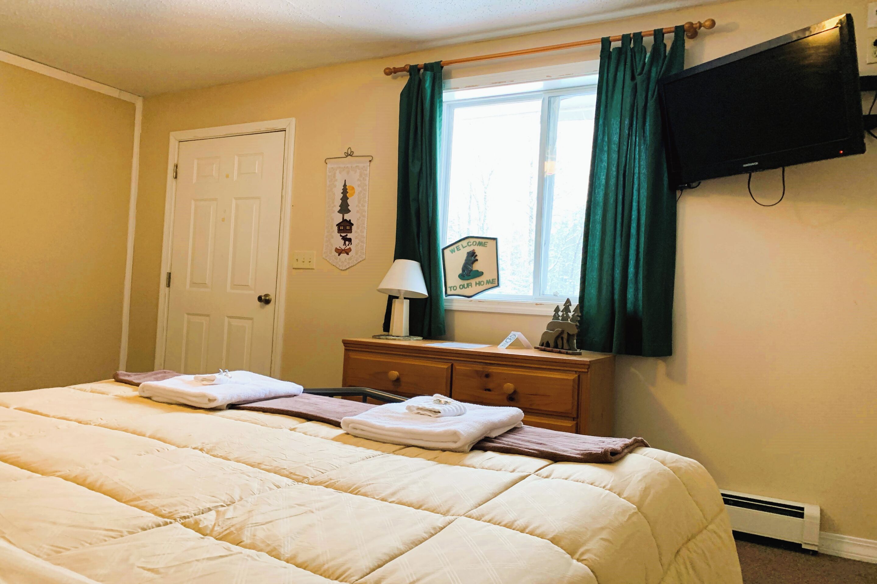 A bedroom with a bed, a dresser, a television, and a window with curtains.