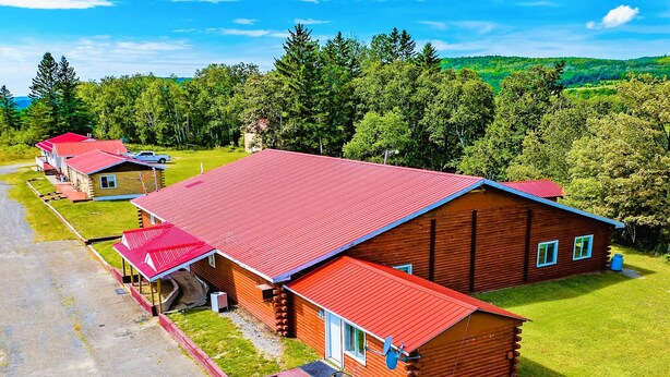 Une cabane en rondins avec un toit rouge, entourée d’une pelouse et d’arbres.