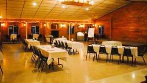 Une salle de banquet avec plusieurs tables rondes et des chaises, un tableau blanc et un ventilateur de plafond.