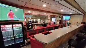 Un espace bar doté d’un long comptoir, de plusieurs téléviseurs diffusant des événements sportifs et d’un réfrigérateur rempli de boissons.