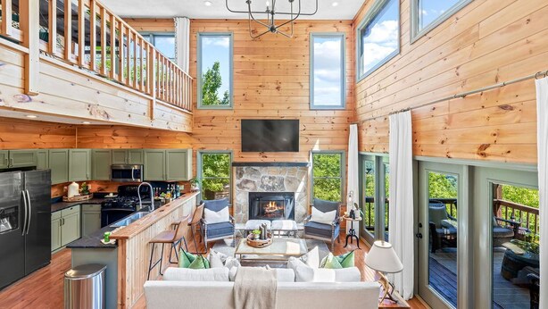 Un amplio salón con chimenea, paredes de madera y ventanas grandes.