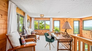 Interior acogedor de una cabaña con paredes de madera, un comedor y ventanas amplias que ofrecen vistas panorámicas.