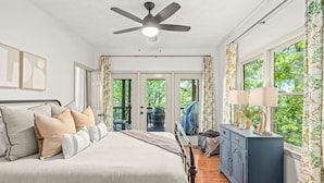 Un dormitorio con cama, ventilador de techo, cómoda y ventana con cortinas.