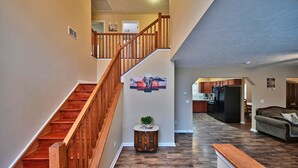 A spacious living area with a wooden staircase, a round side table with a plant, and a kitchen in the background.