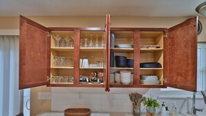 A kitchen with open wooden cabinets containing glassware, plates, and bowls.