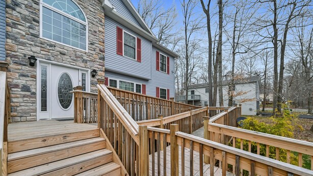 A two-story house with a stone facade, a wooden deck, and a staircase leading to the front door.
