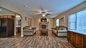A spacious living room with hardwood flooring, two sofas, a coffee table, a fireplace, and a ceiling fan.