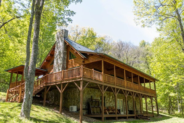 A log cabin with a stone chimney, wooden deck, and a covered porch. - Log Cabin in Wooded Scenery Near Downtown Boone (Boone)
