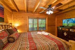 A wooden cabin bedroom with a bed, a television, and a window with blinds. - Log Cabin in Wooded Scenery Near Downtown Boone (Boone)