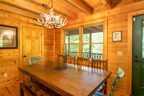 Cozy lodge room with a large dining table and six chairs, a unique chandelier, and framed pictures on the walls.