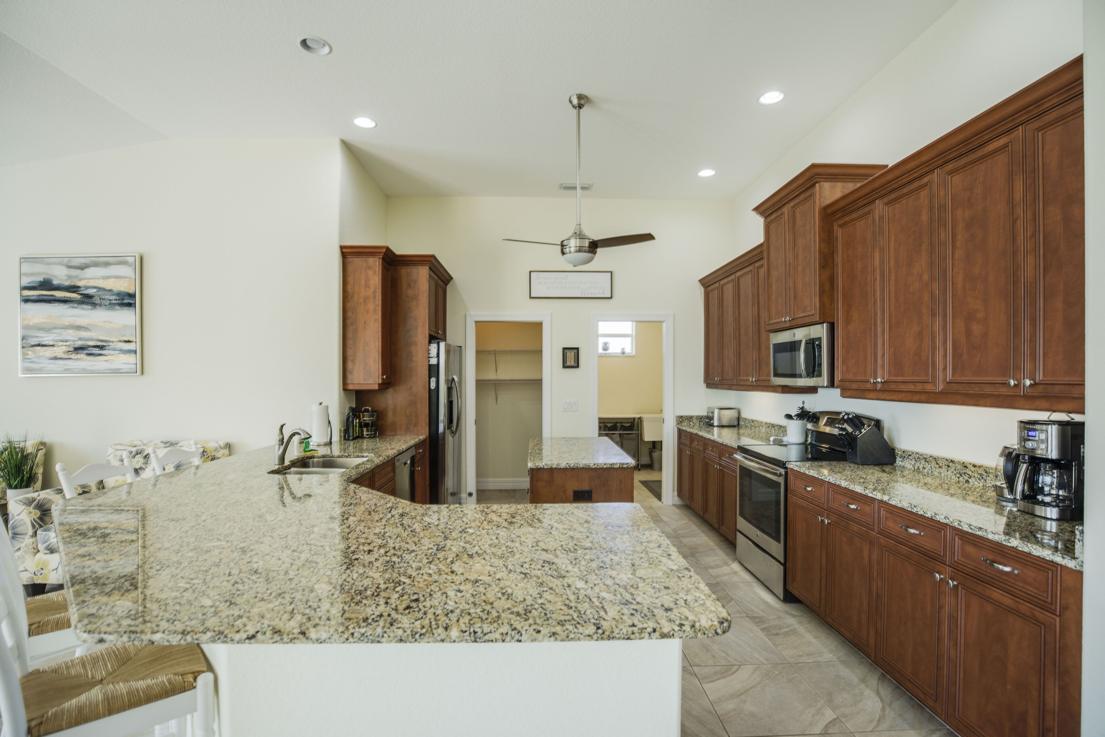 A spacious kitchen with granite countertops, wooden cabinets, stainless steel appliances, and a ceiling fan.