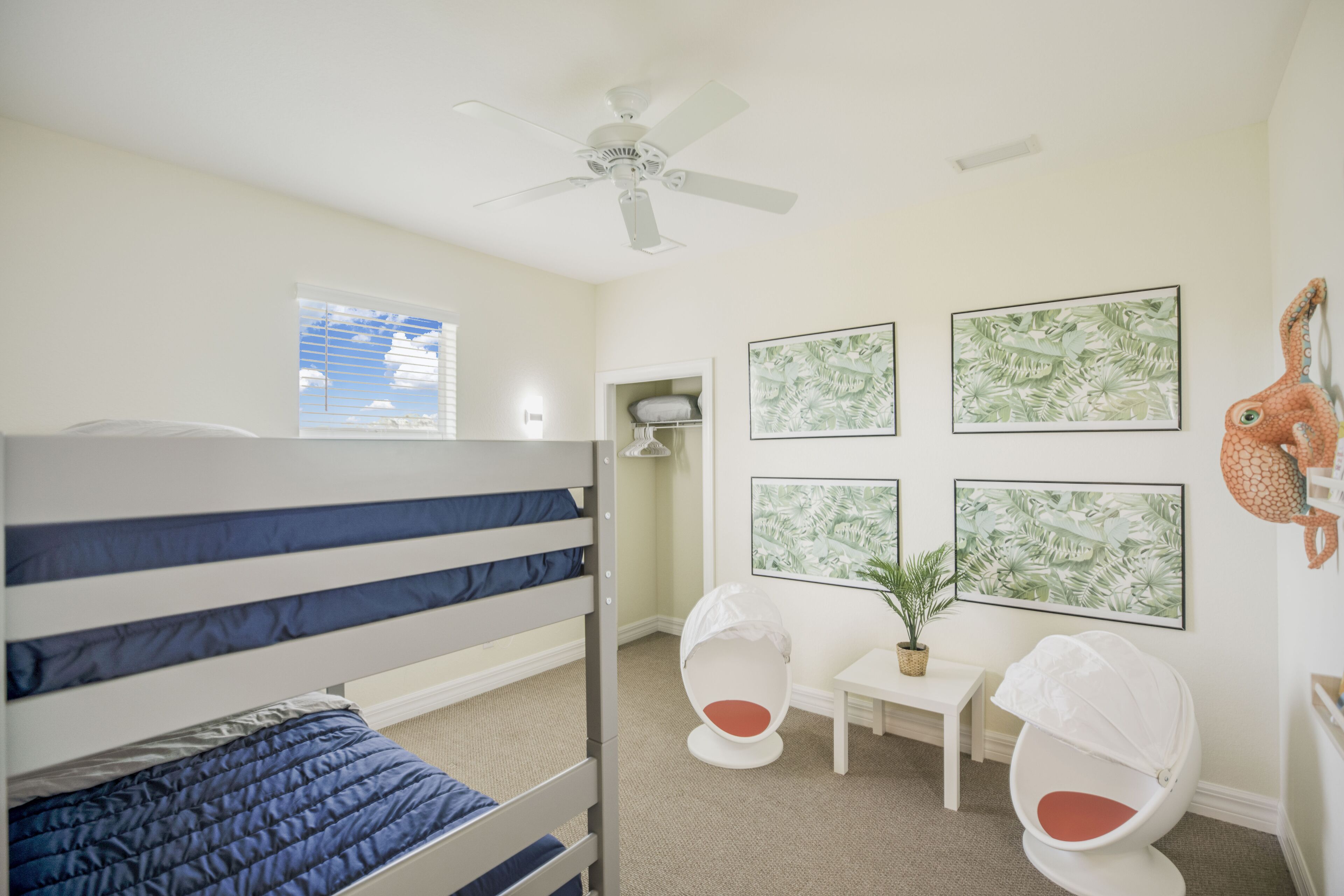 Ein Kinderzimmer mit Etagenbetten, Deckenventilator, kleinem Tisch mit Pflanze und Wandbildern.