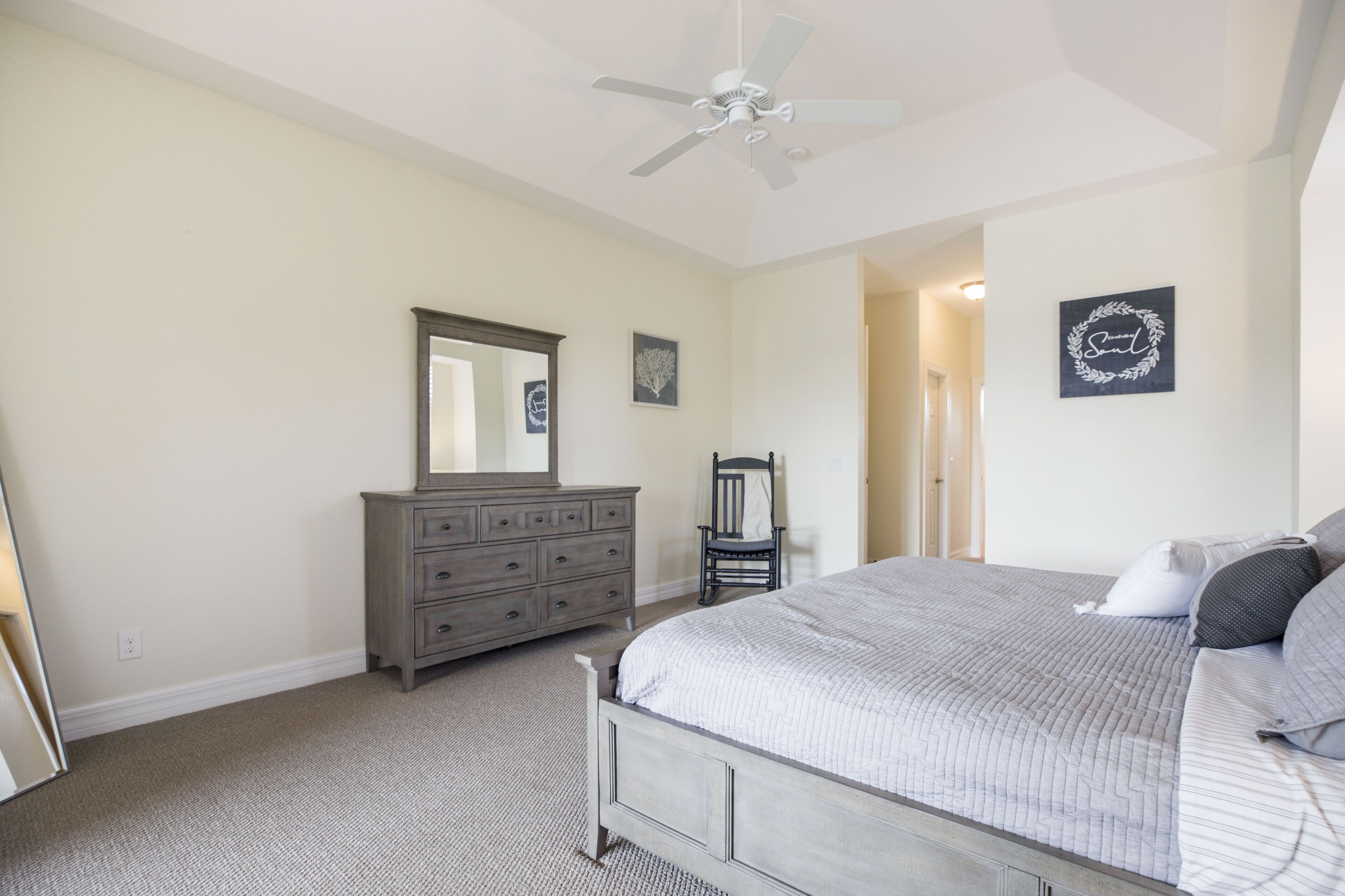 A bedroom with a bed, dresser, chair, and ceiling fan.
