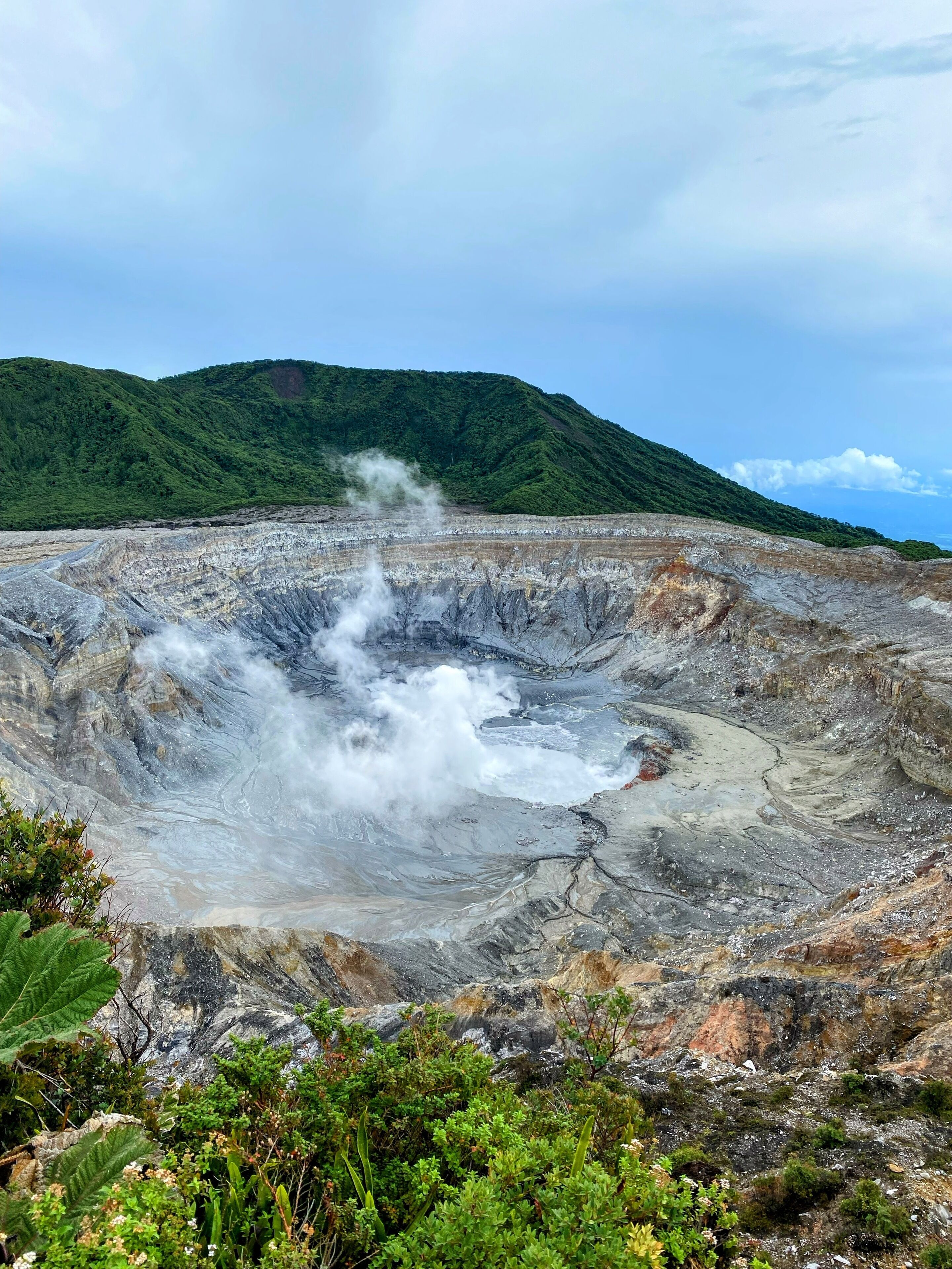 A volcanic crater with steam rising, surrounded by green hills.