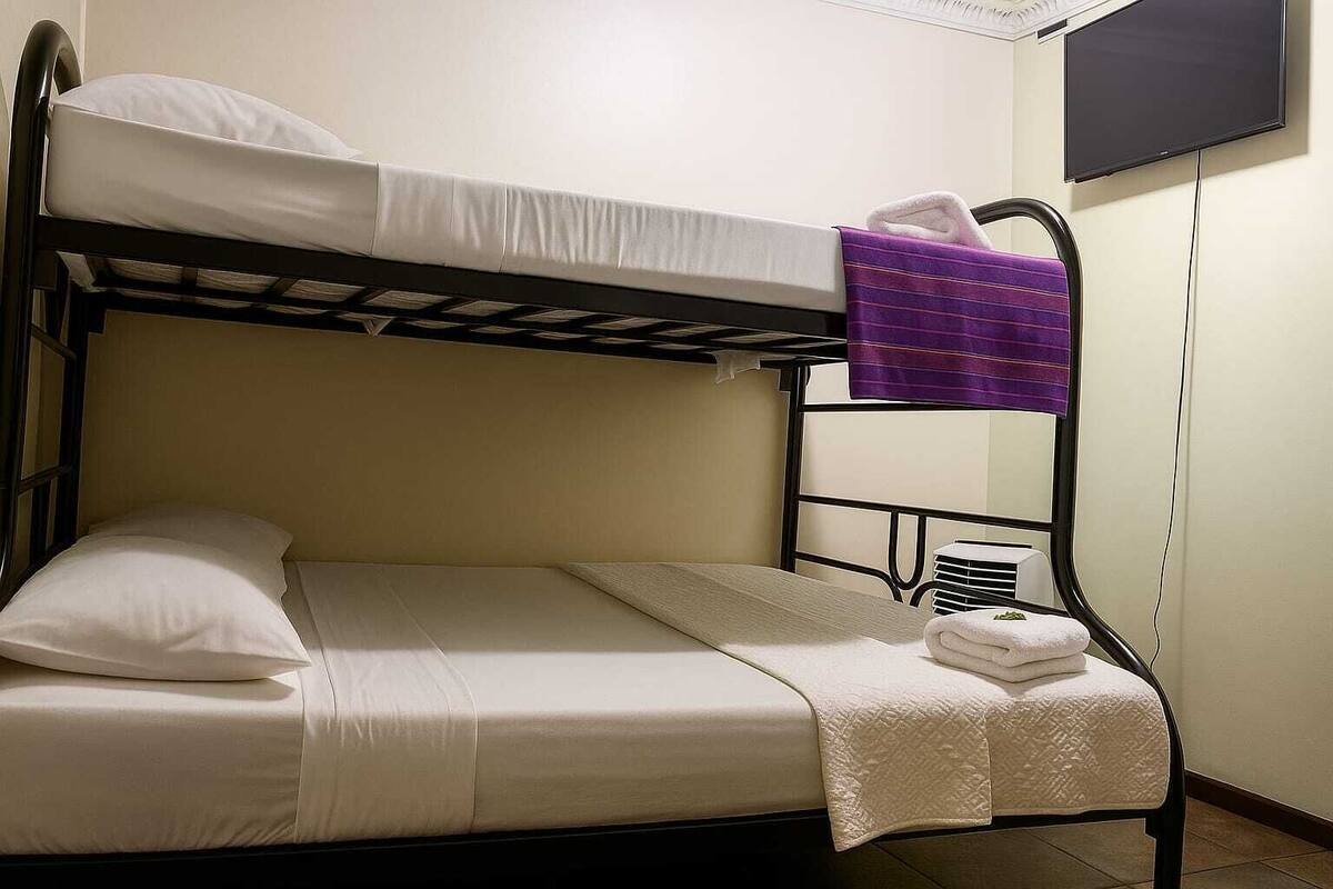 Una cama litera con ropa de cama blanca, una toalla morada y un televisor montado en la pared.