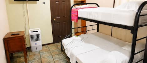 A small, clean room with a bunk bed, a television mounted on the wall, a door, and a small wooden table with a heater.
