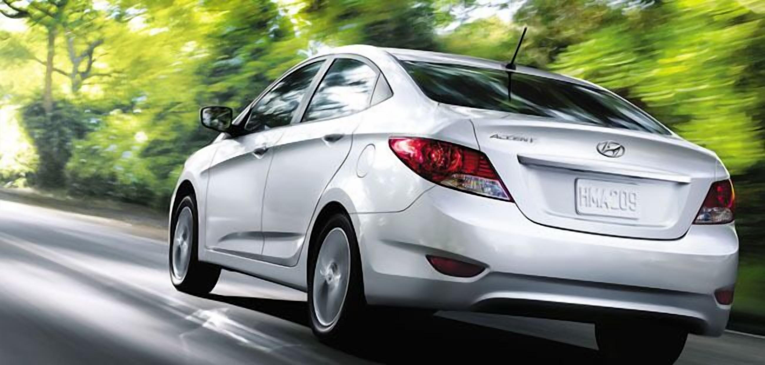 A white sedan driving on a road with trees in the background.