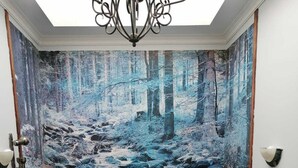 A staircase with a forest mural on the wall, a chandelier, and a wooden handrail.