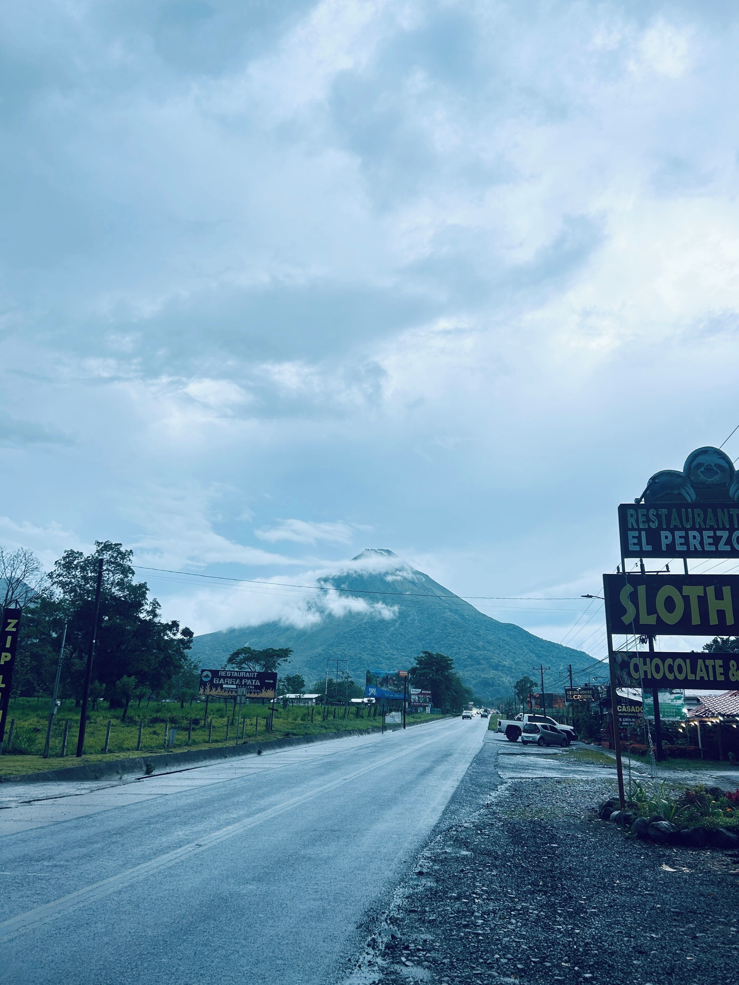 Una carretera con una montaña al fondo y señales de un restaurante y una tienda de chocolate.