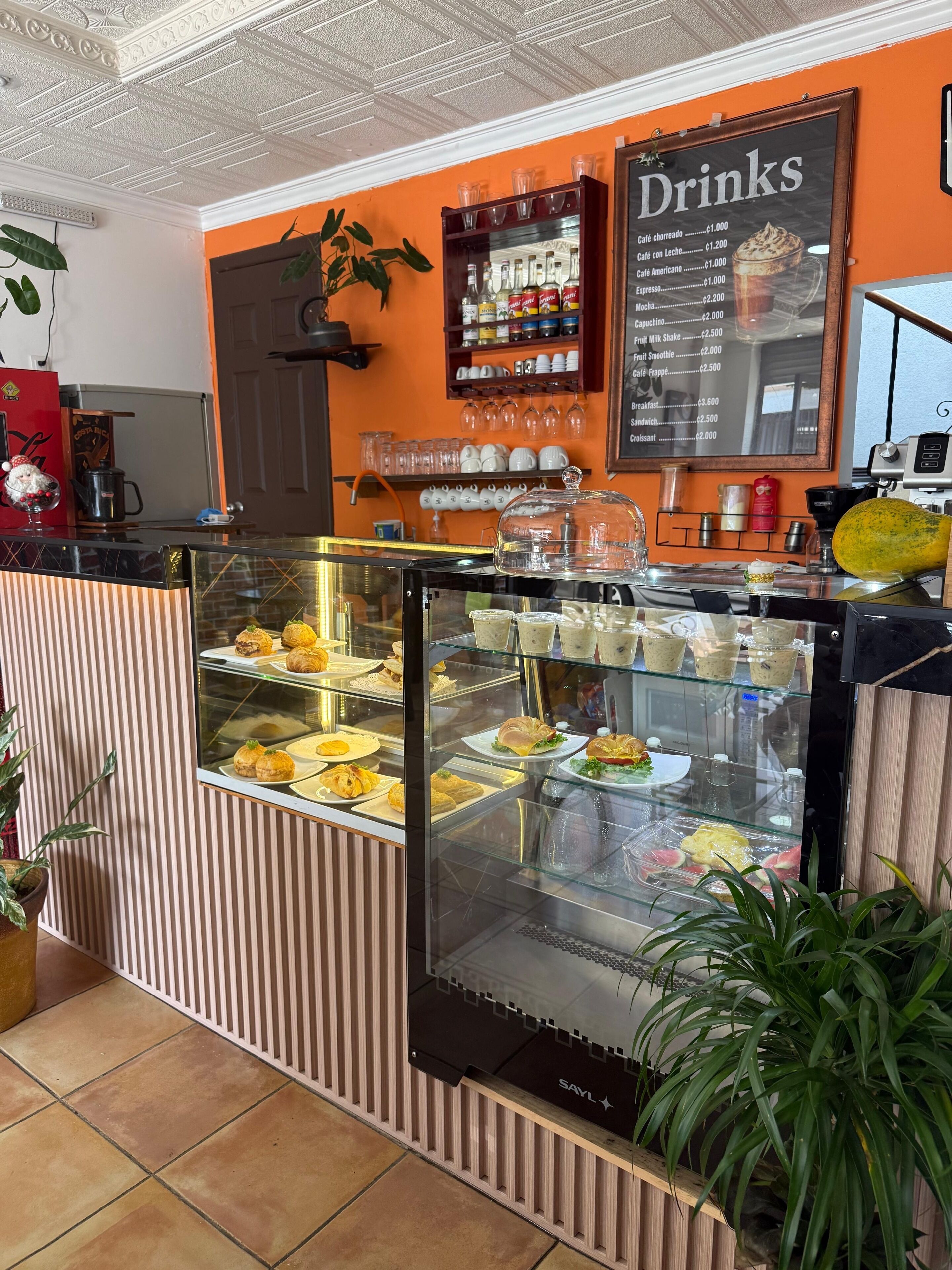 Un café avec un tableau affichant les boissons et les prix, une vitrine remplie de pâtisseries et une machine à café.